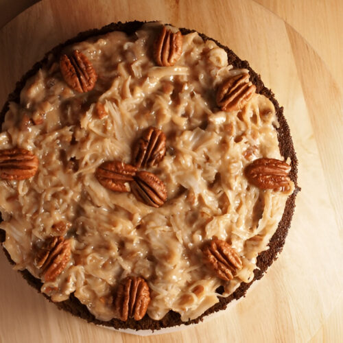 A beautifully displayed German Chocolate Cake with coconut pecan frosting and garnished with toasted pecans and coconut flakes.