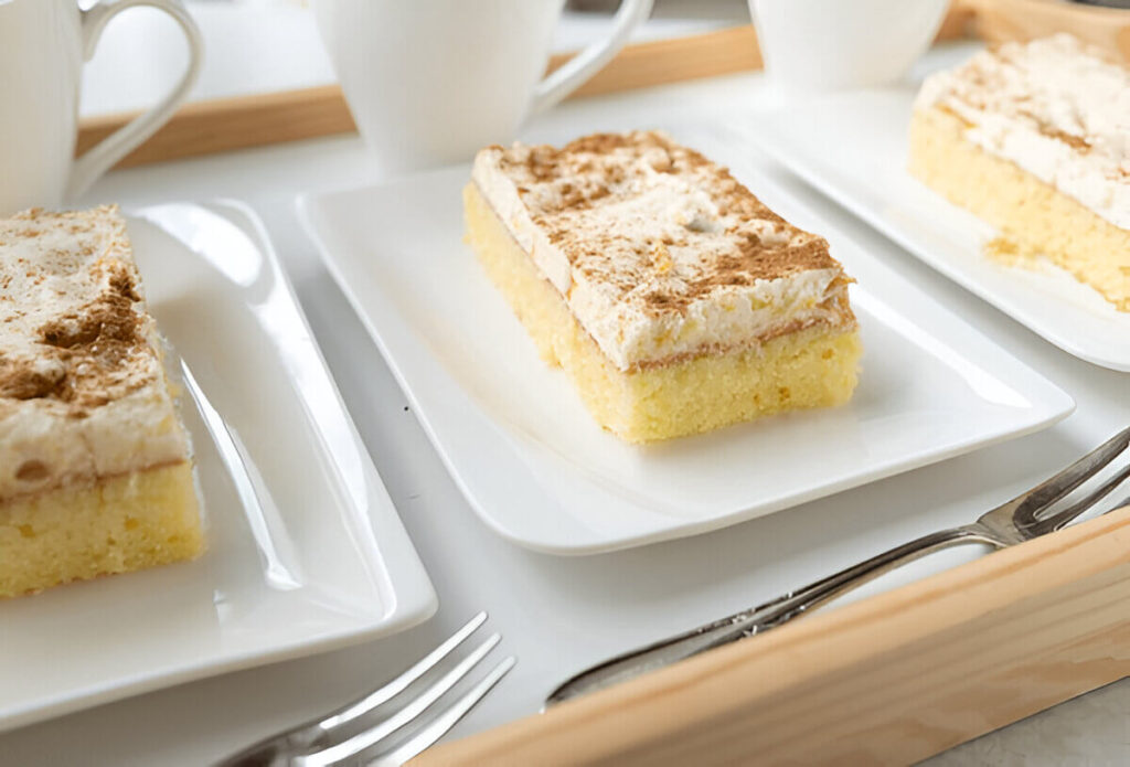 A freshly baked kefir sheet cake, golden brown and cut into squares, served on a plate with a light dusting of powdered sugar.