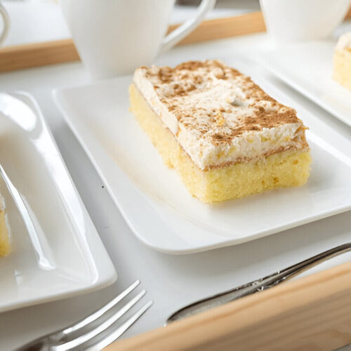 A freshly baked kefir sheet cake, golden brown and cut into squares, served on a plate with a light dusting of powdered sugar.