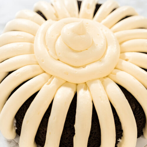 Nothing bundt cake with cream cheese frosting on a white plate with a silver fork.