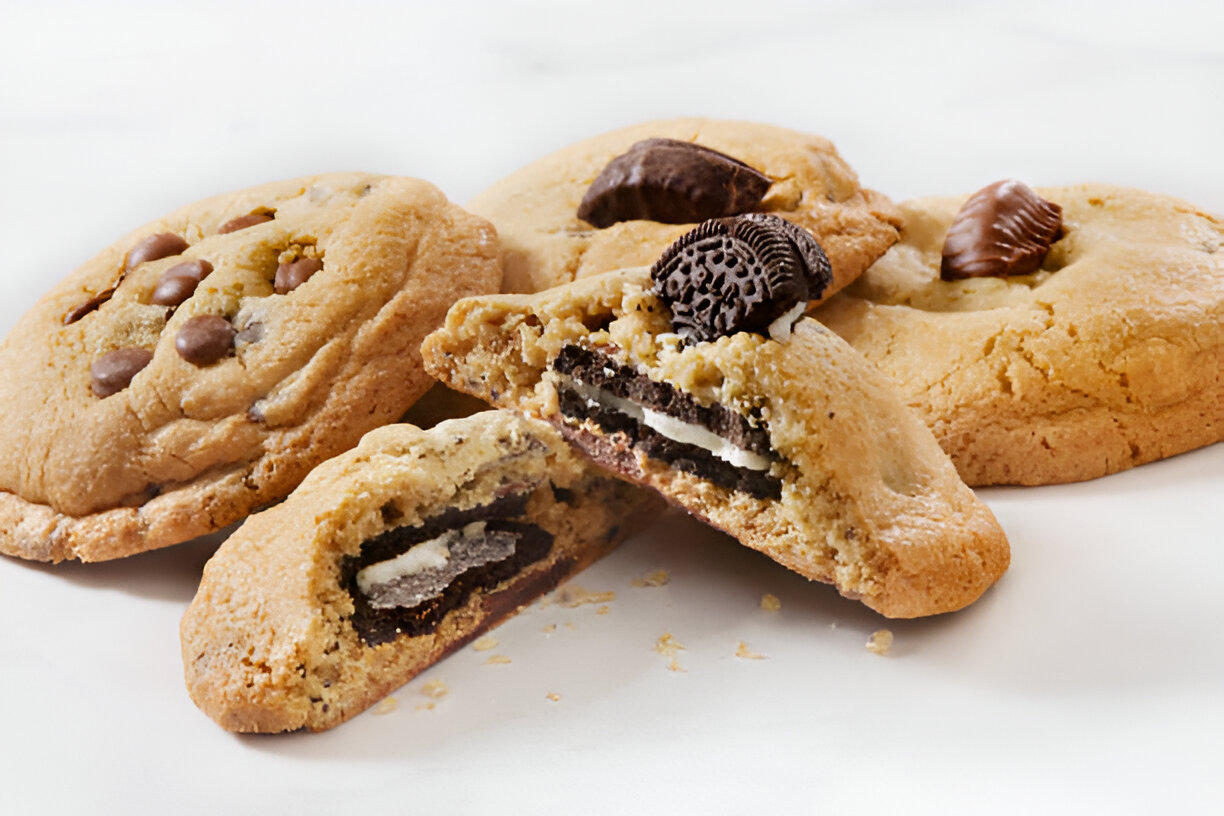 Close-up of a cookies and cream cookie broken in half, showing a soft and chewy center with Oreo pieces.