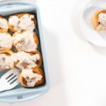 Freshly baked sourdough cinnamon rolls with a creamy glaze in a baking dish.