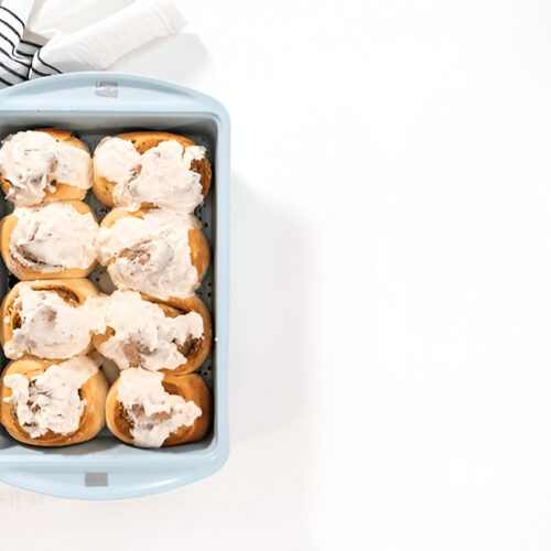 Close-up of sourdough cinnamon rolls in a baking dish, generously topped with cream cheese glaze.