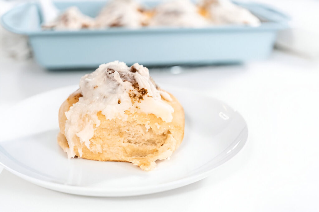 A single sourdough cinnamon roll on a plate with a swirl of cinnamon and cream cheese glaze.